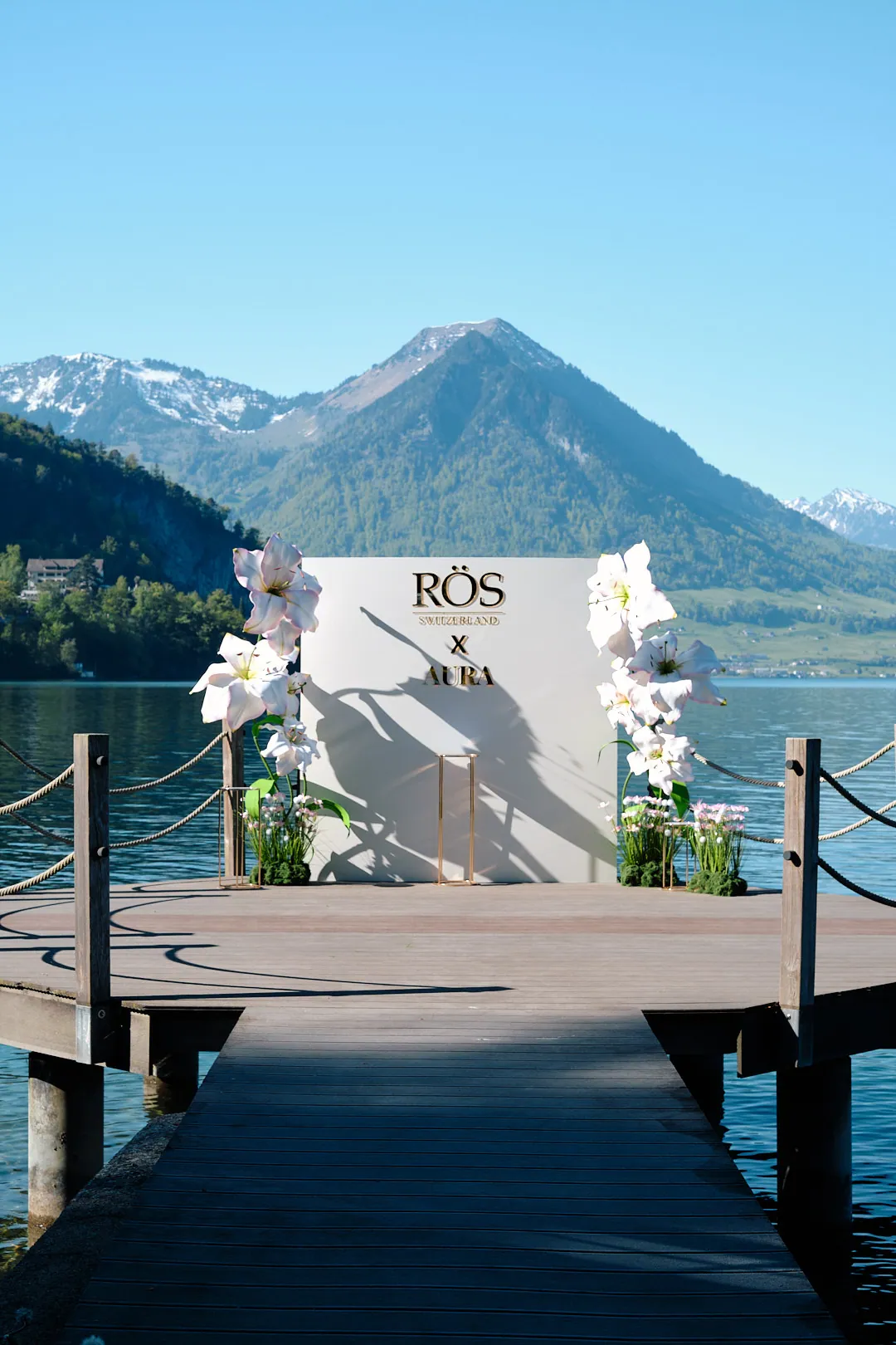 Fotowand RÖS Switzerland x AURA mit weißen Orchideen auf dem Steg am Vierwaldstättersee