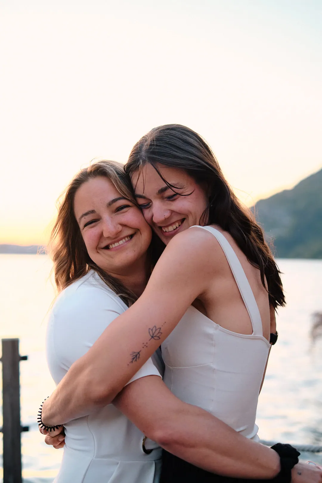 Zwei Frauen umarmen sich lachend im Abendlicht am See