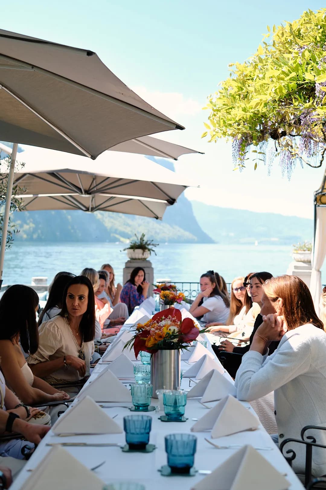 Lange Tafel mit Blumen auf der Terrasse, dahinter See und Berge