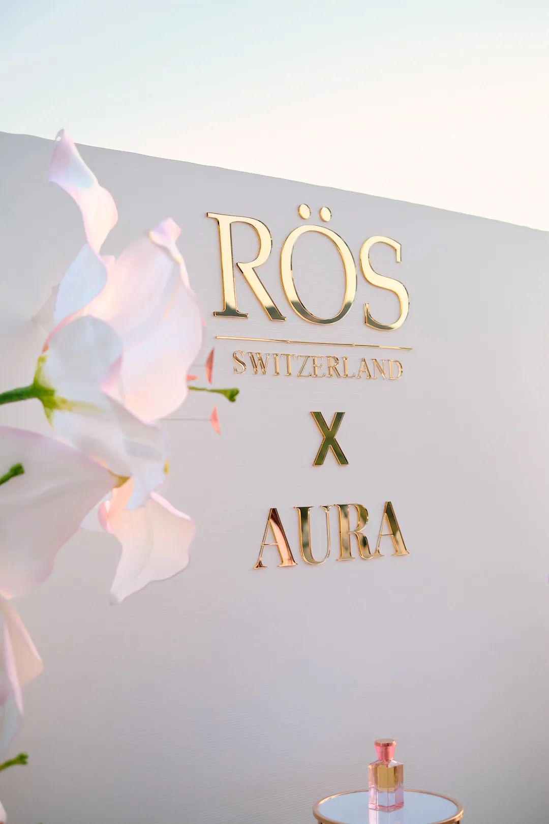 Fotowand RÖS Switzerland x AURA mit weißen Orchideen, davor ein Parfum-Flakon von RÖS