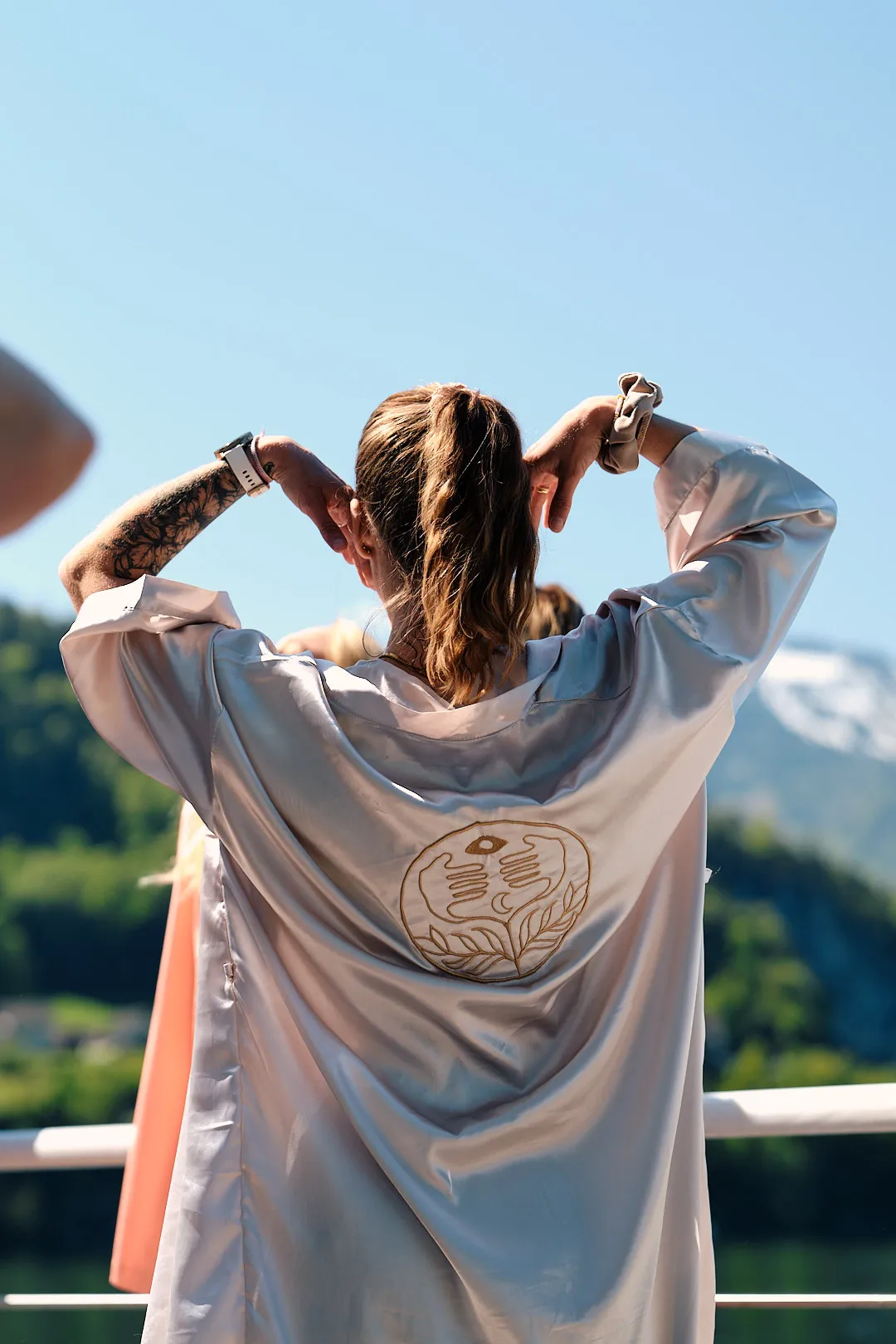 Rückenansicht einer Teilnehmerin im Satin-Kimono mit gesticktem goldenem Emblem vor See und Bergen