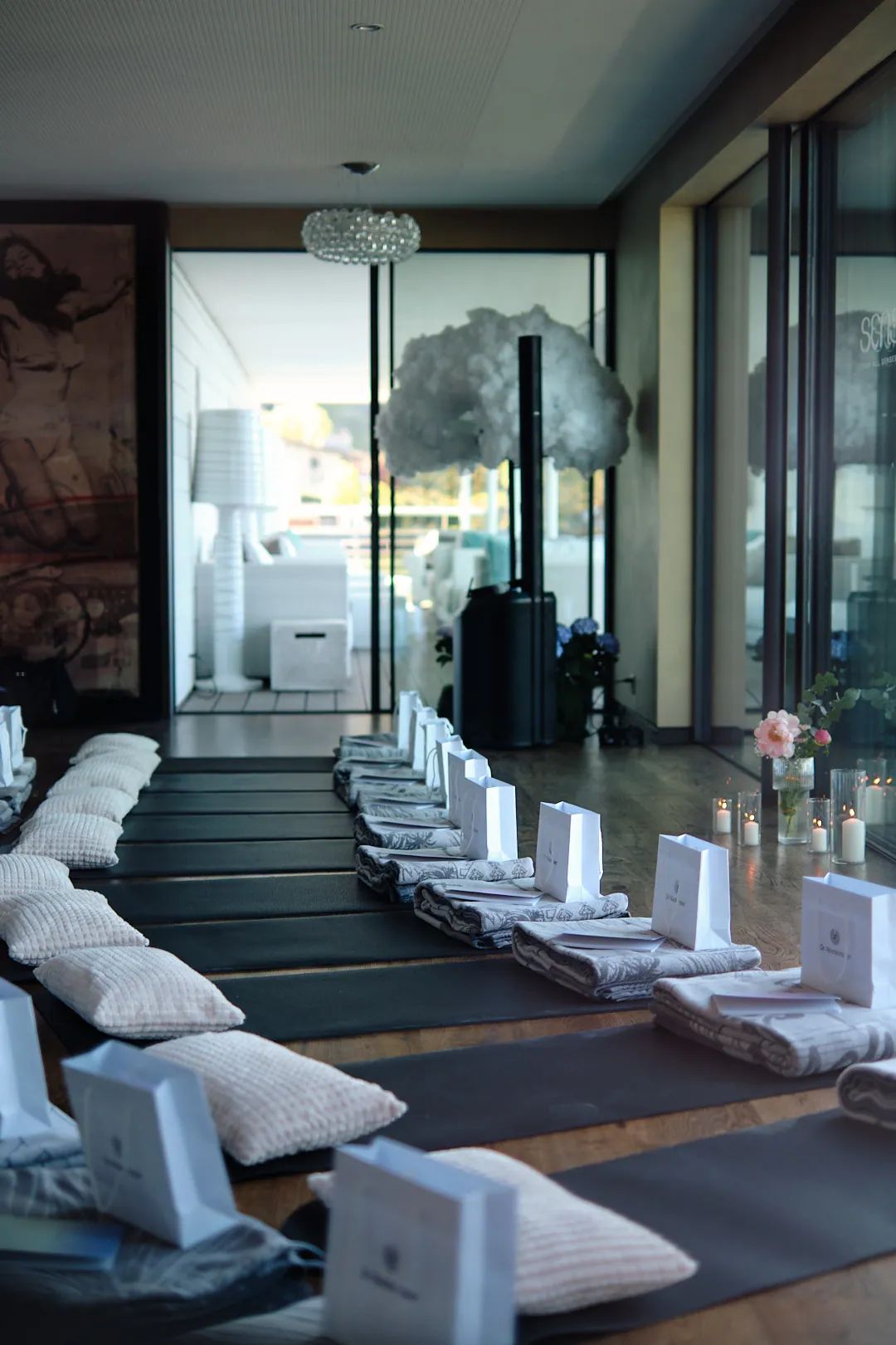 Vorbereiteter Raum mit Sitzkissen, Kerzen und weißen Taschen vor großen Fenstern am Vierwaldstättersee